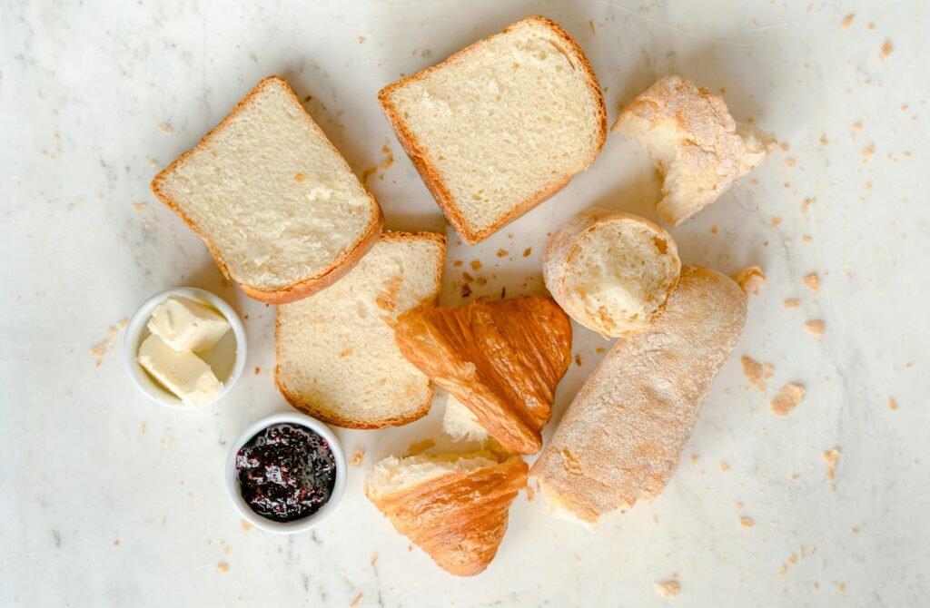 Delicious variety of breads including croissants with butter and jam on a marble surface.