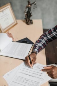 Hands of a person signing official documents on a desk in an office setting.