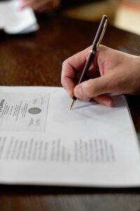 A detailed close-up photo of a hand signing a formal document with a pen, creating a professional agreement.